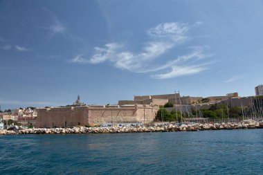 Bir teknenin bakış açısından, Marsilya 'nın ikonik limanı şehrin tarihi mimarisi ve derin mavi gökyüzü tarafından çerçevelenmiş yatlar ve yelkenlilerle doludur. Kompozisyon sükuneti iletiyor ve Akdeniz atmosferini çağrıştırıyor, 