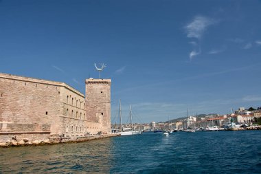 Bir teknenin bakış açısından, Marsilya 'nın ikonik limanı şehrin tarihi mimarisi ve derin mavi gökyüzü tarafından çerçevelenmiş yatlar ve yelkenlilerle doludur. Kompozisyon sükuneti iletiyor ve Akdeniz atmosferini çağrıştırıyor, 