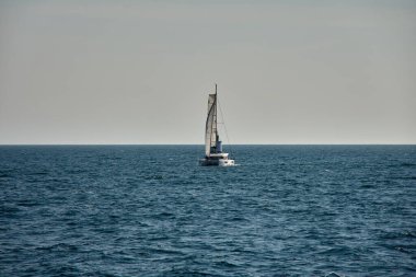 Yelkenlisi olan bir yelkenli Vigo Estuary 'nin açık sularında sorunsuzca ilerler ve deniz fenerine yaklaşır. Gökyüzü yumuşak, berrak bir atmosfer sunarken deniz, çerçevenin büyük bir kısmını mavi tonlarda kaplar..