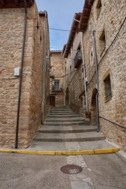 Teruel 'in Puertomingalvo kasabasındaki küçük taş evler arasında dar, kaldırım taşı gibi bir sokak esiyor. Atmosfer, rengarenk saksılar ve balkon detaylarıyla vurgulanan barış ve kırsal özgünlüğü taşır. 