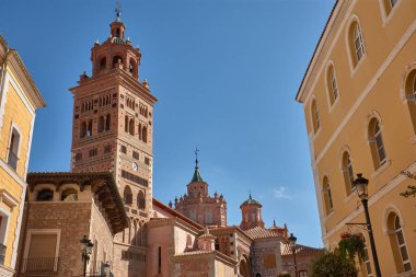 Teruel 'deki Santa Maria de Mediavilla Katedrali kırmızı tuğla, süs pencereleri ve metal bir haçla taçlandırılmış yeşil kubbe ile Mudejar tarzında yükselir. Mavi gökyüzü malzemelerin dokusunu vurgular ve dinginliği taşır. 