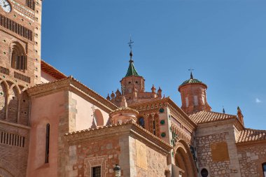 Teruel 'deki Santa Maria de Mediavilla Katedrali kırmızı tuğla, süs pencereleri ve metal bir haçla taçlandırılmış yeşil kubbe ile Mudejar tarzında yükselir. Mavi gökyüzü malzemelerin dokusunu vurgular ve dinginliği taşır. 