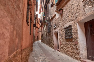 Albarakin, İspanya - 6 Eylül 2025, Albarakin kasabasında dar ve sık sık dik bir cadde, kırmızı ve koyu renkli cepheleriyle karakterize edilen geleneksel evler arasında, ahşap ve işlenmiş demir balkonlarla yükselir.. 