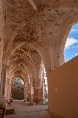 The vaulted corridors of the Cloister of Our Lady of Piedra in Aragon, Spain, highlight the robust Gothic architecture and the patina of time on its stones. The soft light and warm tones of the stone create an atmosphere of solemnity and mystery, whi