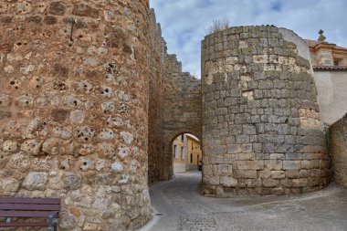 Medieval stone walls in the city of Uruena, Valladolid, with an entrance arch leading into the town streets. The textures of the stones highlight the history and cultural heritage, while the contrast with the yellow houses creates an authentic