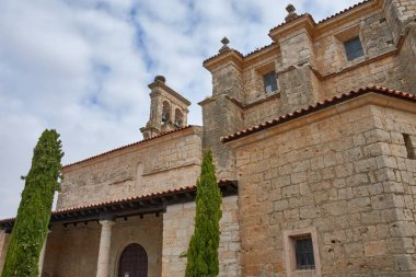 The 16th-century Church of Our Lady of Azogue in Uruena, Valladolid, Spain, with its massive stone facade, columned arcades, and a distinctive stork's nest atop what appears to be a Bell tower. 
