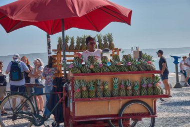Nazare, Portugal - September 16, 2025,A Black woman runs a street stall selling pineapples and juice in Nazare, Portugal, under a red umbrella that stands out among the warm tones of the surroundings. 