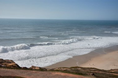 Yüksek enerjili bir deniz ortamında, bir uçurumdan Nazare, Portekiz 'in dev dalgalarına meydan okuyan çok sayıda sörfçü görülebilir. Derin mavi okyanus, beyaz köpük ve hareket eden insan figürleri arasındaki zıtlık güçlü bir... 