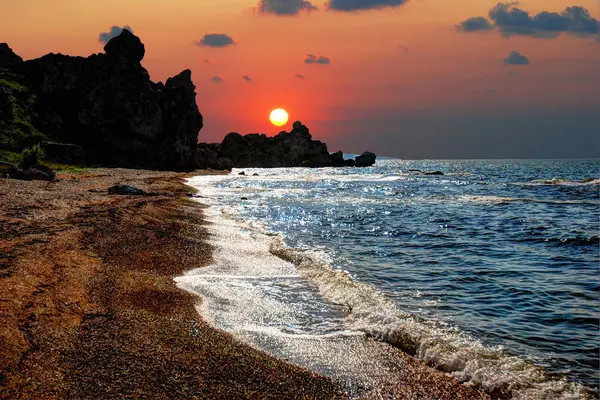 Kayanın üzerinde gün batımı. Akşamları deniz dalgaları. Siyah kayaların üzerinde güneş.