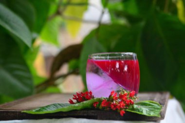 Justicia Spicigera İçeceği, Tahta Tahtadaki Buzlu Cam Kırmızı Çiçekler ve Yeşil Yapraklar, Buzlu Justicia Spicigera İçecek, Tahta Masada Kırmızı Çiçekli Cam ve Yeşillik