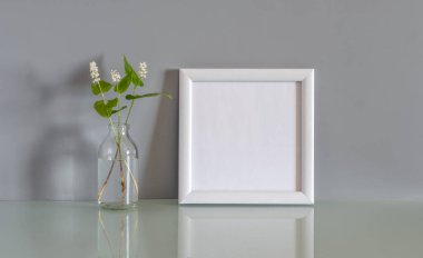 Beyaz ahşap fotoğraf çerçevesi ve gri arka planda bir buket çiçek.
