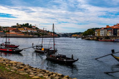 Üç kahverengi sersemletici geminin olduğu nehir, arka planda şehrin manzarası ve uzaklıktan bir köprü görülebiliyor.