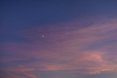 Güzel bir akşam gökyüzü mor ve pembe renklerle boyanır, hilal şeklinde bir ay sergilenir. Huzurlu sahne bir sükunet ve sükunet hissi uyandırıyor..