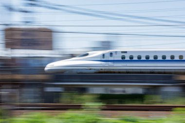Japon Nozomi Shinkansen Mermi Treni Nagoya İstasyonu 'ndan ayrılırken hızla geçiyor. Hareket bulanık arkaplan trenin hızını vurguluyor ve parlak aerodinamik tasarımını vurguluyor.