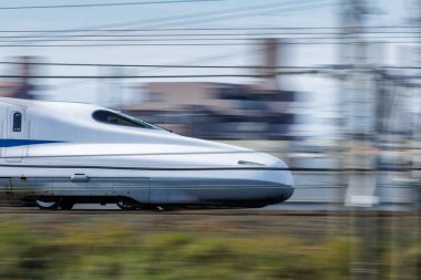 The long, or duck-bill nose of Japan's Nozomi Shinkansen Bullet Train speeds by a motion blurred background heading for Nagoya Station. The train operator's cap is visible in the tinted windows. clipart