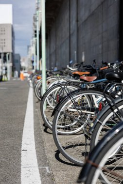 Park halindeki bir sıra bisiklet Japonya 'nın Nagoya kentindeki küçük bir tren istasyonuna ulaşan sakin bir kenar sokak hizasında. Sahne, bisiklet sürmenin yaygın bir ulaşım biçimi olduğu işlek bir şehir alanını gösteriyor.