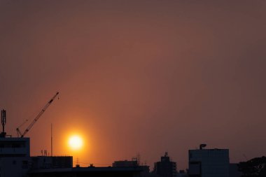 Kar bulutları şafağın ufuk turuncusunu maskeliyor. Yumuşak, puslu bir güneşle benekli. Siluetli şehir manzarası üzerinde rüya gibi bir zemin oluşturuyor..