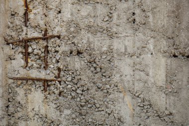 Paslı demir ızgara çıkıntıları bitmemiş, yıpranmış beton bir duvardan çıkar, duvarın kaba monoton gri yüzeyinde turuncu kahverengi renkli bir tik-tac-toe matrisi oluşturur, çeşitli küçük taşlardan oluşan doku..