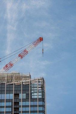 Kule vinci, üzerinde cam paneller ve iskeleler bulunan modern gökdelenin üzerinde uzanıyor. Ed ve beyaz kolu açık mavi gökyüzüne uzanır ve kentsel gelişimi gösterir..
