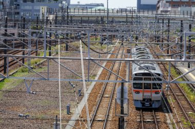 Tren, kentsel bir ortamda karmaşık bir tepe ve metal şebekeler ağı altında bekliyor, hareketli bir geçiş demiryolu sisteminin altyapısını vurguluyor..