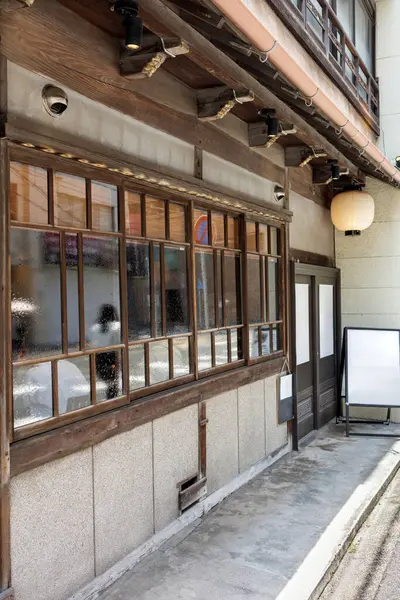 Geleneksel stil ahşap cepheli Japon restoranında öğle yemeği yiyen restoran müşterilerinin figürleri, yoldan geçen insanların figürlerini yansıtan büyük cam pencereler olarak görülüyor..