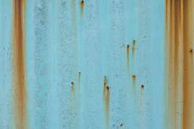 Paslı çizgiler, aşınmış ve boyanmış bölgeler arasında kontrast oluşturan açık mavi yıpranmış bir yüzeyde dikey olarak ilerler. Yaşlanmış yüzey işaretleri, oksitlenme etkileri ve soyut elementleri gösterir.