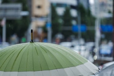 Yağmur fırtınası sırasında açık yeşil ve kapalı beyaz şemsiyeli, su damlacıkları tırtıklı yüzeye yapışmış. Arabalar, binalar ve bariz yağmurla Bokeh Şehri 'nin arka planına kurulmuş..