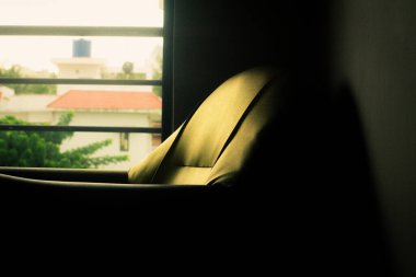 Loş bir odada pencerenin yanında basit bir tahta sandalye oturuyor. Pencere camı duvarda belli belirsiz bir parıltı bırakıyor..