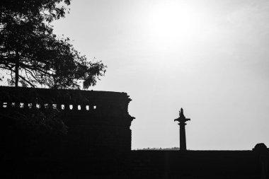 Alacakaranlık gökyüzüne dayanan basit bir haçın fotoğrafı. Saat kulesi olan karanlık bir binanın tepesine monte edilmiş.