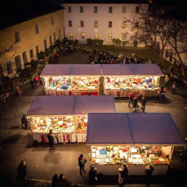 A wide shot photo from a high angle of a holiday market in front of a historic house, with stalls decorated for Christmas and a backdrop of twinkling lights, using soft focus to create a joyful, holiday atmosphere clipart