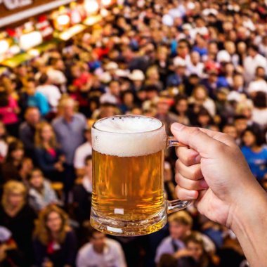 A cowboy shot of a hand holding a traditional Oktoberfest beer mug, viewed from above, with the lively crowd and festive decorations softly blurred in the background clipart