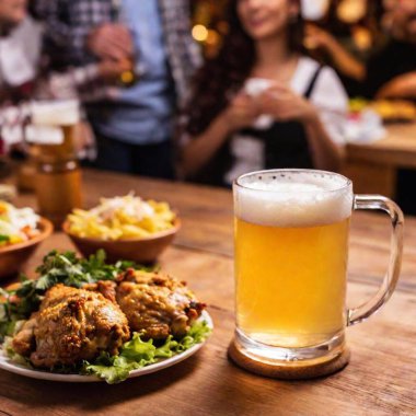 A high angle shot of a frothy beer mug being placed on a table, with Oktoberfest decorations and a lively crowd softly fading into the background clipart