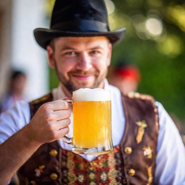 young man holding a mug of beer and a beer in the oktoberfest. clipart