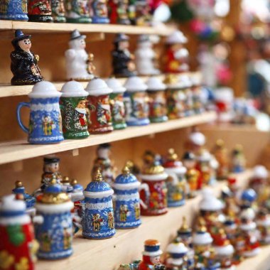 lose-up image of traditional Bavarian souvenirs, such as miniature beer steins and alpine hats, displayed at a stall in Munich Oktoberfest. The rack focus shifts from the souvenirs to the bustling fairground beyond, all captured at eye leve clipart