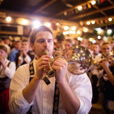 Extreme wide shot capturing the energy of a Bavarian folk music band at Oktoberfest, with a close-up focus on the bell of a trumpet as it gleams under the tent lights. The band and crowd blur slightly, emphasizing the instrument. clipart