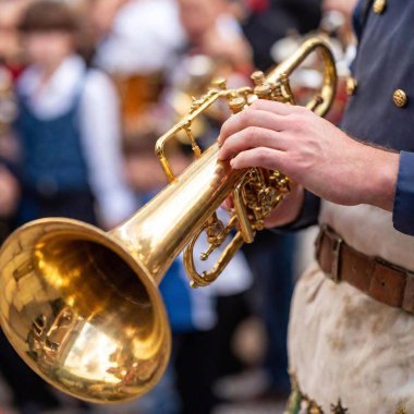 Extreme macro shot capturing the energy of a Bavarian folk music band at Oktoberfest, with a close-up focus on the bell of a trumpet as it gleams under the tent lights. The band and crowd blur slightly, emphasizing the instrument. clipart