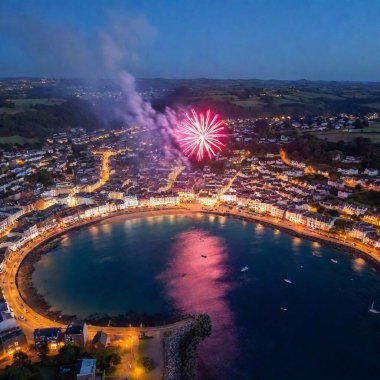 A full shot (FS) aerial view of a coastal town celebrating Bonfire Night, with fireworks reflecting off the water. The deep focus captures the entire scene, including the fireworks, the bonfire on the beach, and the town illuminated buildings. clipart