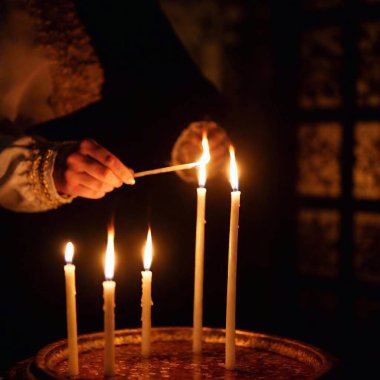 Candle lighting for Yom Kippur: Eye-level full shot of a person in traditional attire lighting a candle, with deep focus capturing the rich details of the ritual setting. clipart