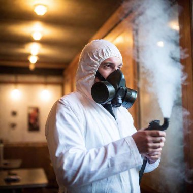 I need a graphic showing a man using the SM Bure ULV fogger device. He directs the stream of steam onto the walls, playing them with steam. This man is to be dressed in a suit protecting against chemical substances and a gas mask. This is a DDD clipart