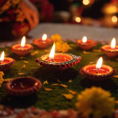 Create an image of a Diwali prayer ceremony from a ground-level angle, using an establishing shot with rack focus. Begin with sharp focus on a diya flame in the foreground, then transition to the family praying in the background clipart