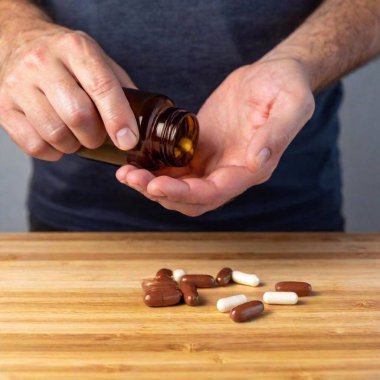 the hand of the doctor holds a pills with a wooden spoon and capsules on a white table. clipart