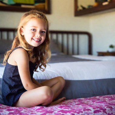 Photo of a beautiful 6 year old white girl, She is dressed in a black bikini. Playing on her bed clipart