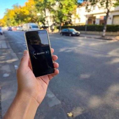 hand holding smartphone with blank white screen on blurred street clipart