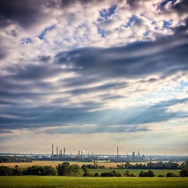 A landscape featuring oil refineries and drilling rigs, with smoke rising into the sky. The scene should be in a wide format, capturing the industrial elements against the backdrop of a natural landscape. The sky is partially cloudy with smoke clipart