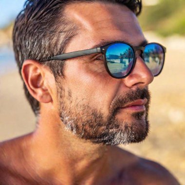 A close-up photo of a Caucasian male adult with sunglasses reflecting the ocean view, deep focus on his face and the texture of the sand grains on his skin, eye-level shot highlighting his relaxed smile and carefree beach day clipart