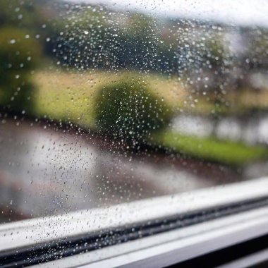 A medium wide shot of a window covered in rain, viewed from a Dutch angle. The shallow focus highlights the raindrops on the glass and the blurred cityscape or landscape outside, with the tilted perspective creating a dramatic effect. clipart