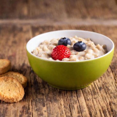 A creative breakfast for kids featuring an oatmeal bowl decorated with a smiley face made from blueberries and strawberries, with a side of toast soldiers clipart