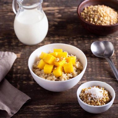 A refreshing breakfast setup with a bowl of quinoa porridge, topped with fresh mango cubes, coconut flakes, and a drizzle of almond milk clipart