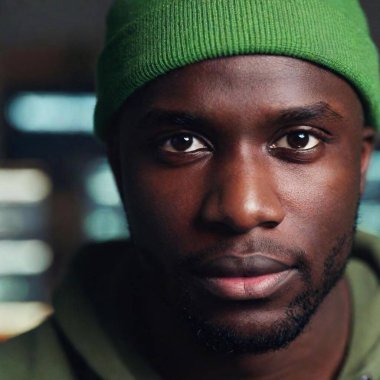 A close-up, eye-level portrait of a black male hacker in a dimly lit room, with his face in sharp focus and the background filled with blurred computer monitors, highlighting the intensity and secrecy of his work clipart