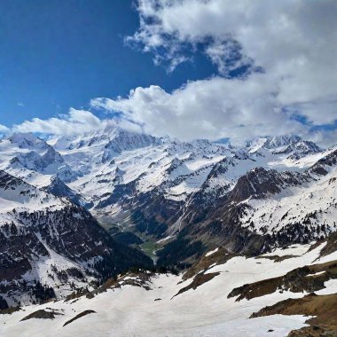 A full shot of a mountain range at eye level, with snow-capped peaks and a lush valley below. clipart